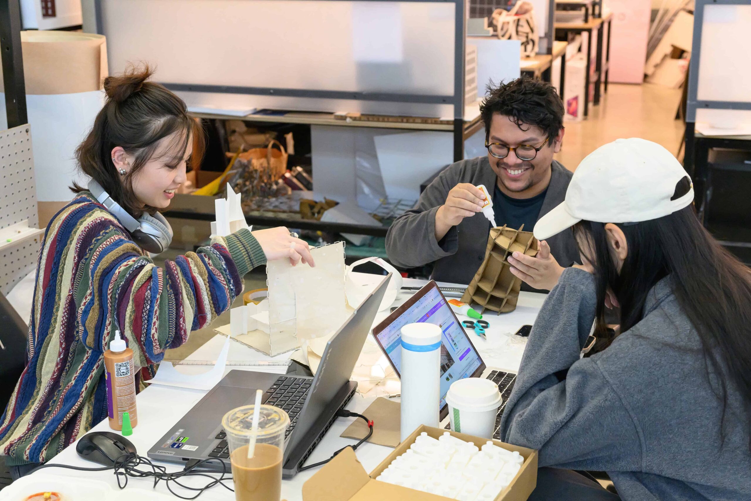 Three students gathered around a table working on projects or laptops