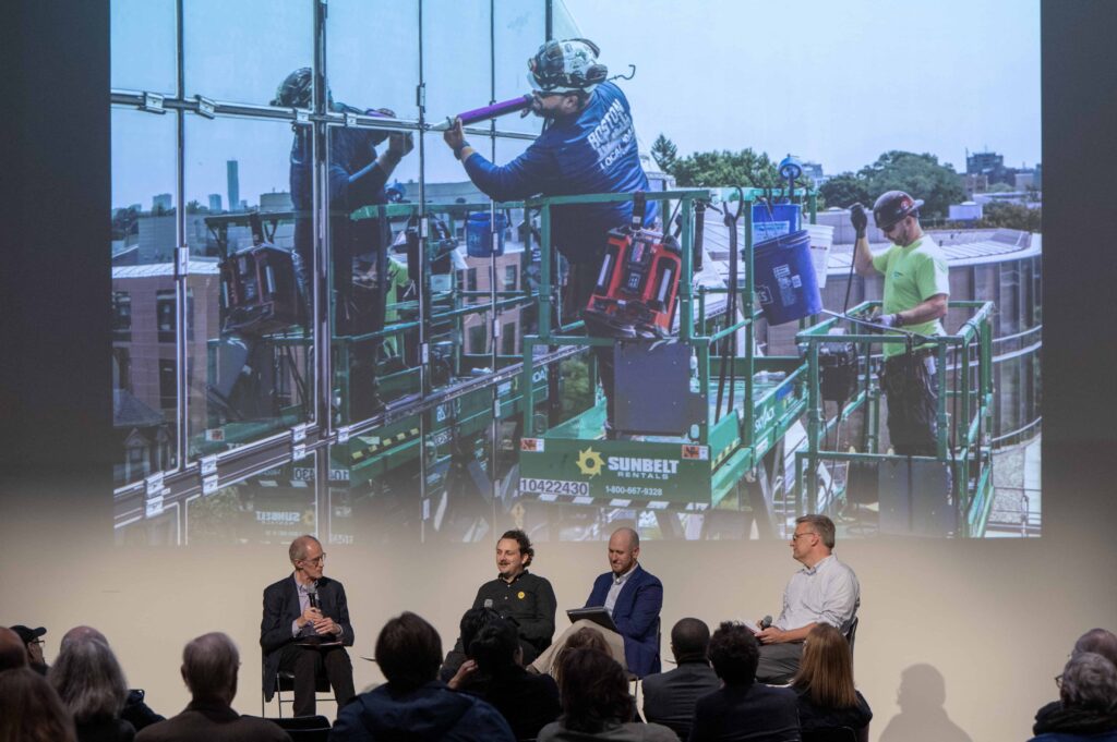 Panel of four speakers on stage with image of Gund Hall windows in background