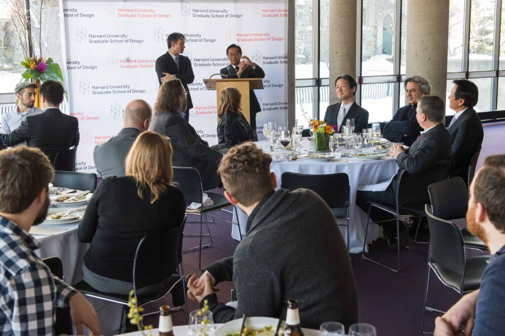 Two people from Takenaka stand near a podium in front of a room of people