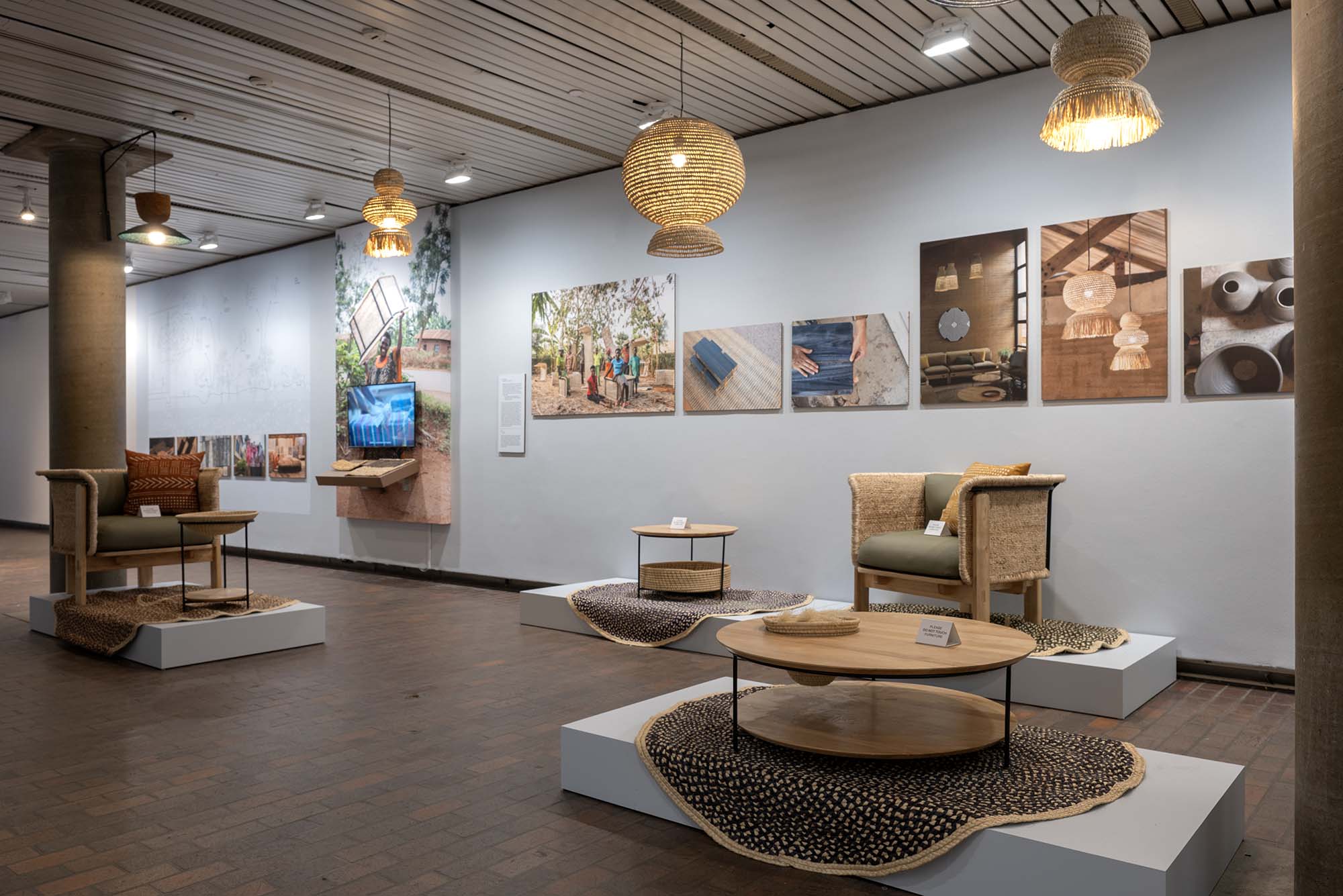 A display of Rwandan furniture on plinths , with photos of other furniture and crafts behind them.