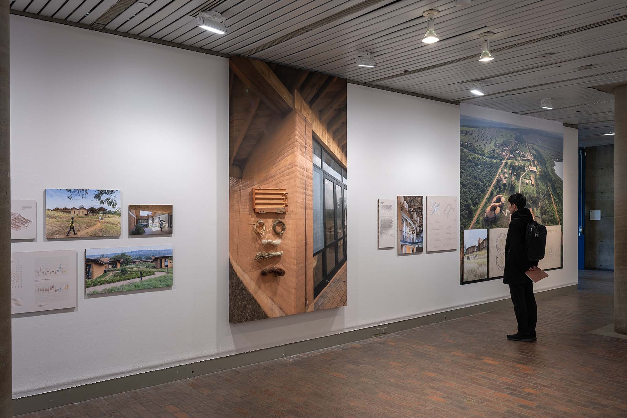 A person studies a photo in an exhibition of large aerial, photos, architectural drawings, and material samples.