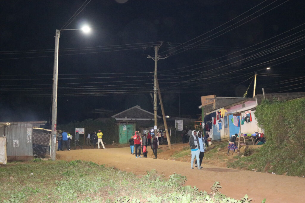 People at night gathering under a tall light pole.