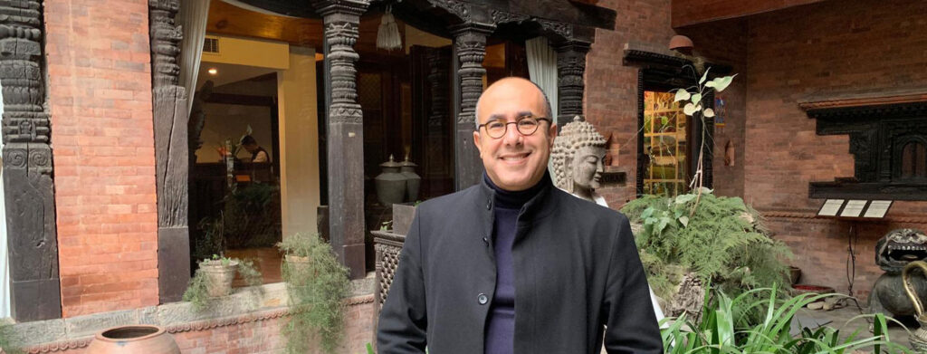 Man smiling in front of brick building.