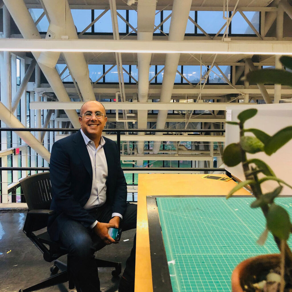 Man sitting at drafting desk with glass and steel framing in the background.