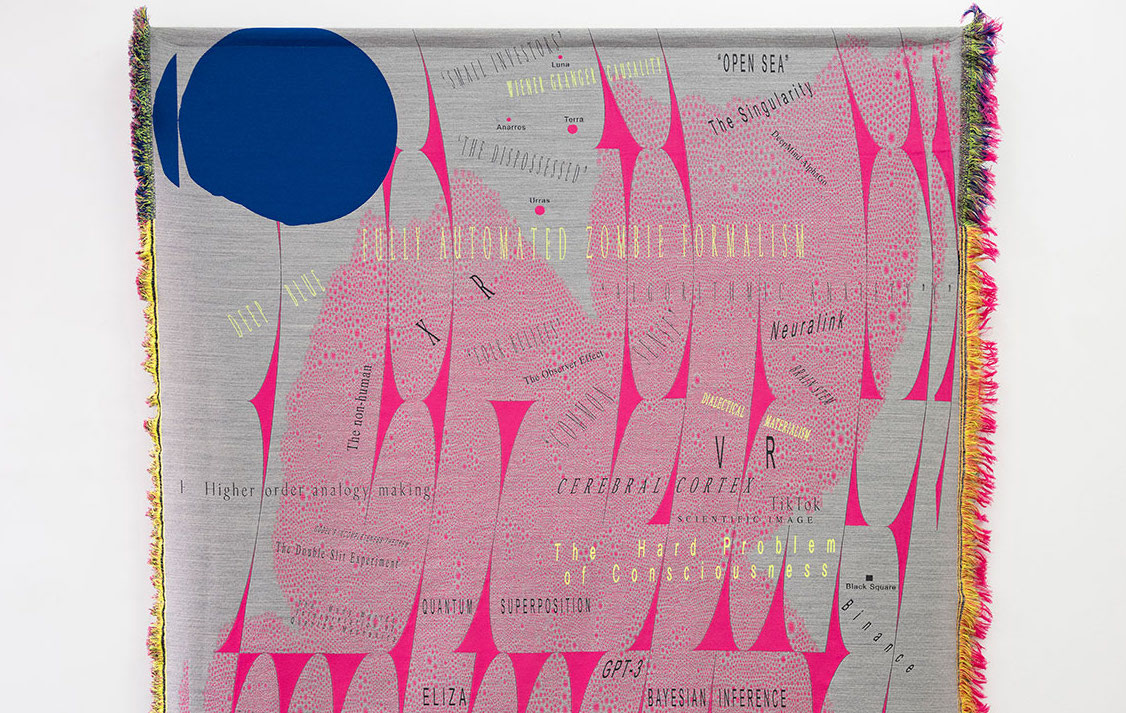 Detail of a fabric tapestry with pink and blue shapes on a gray background and words in different typefaces and colors.