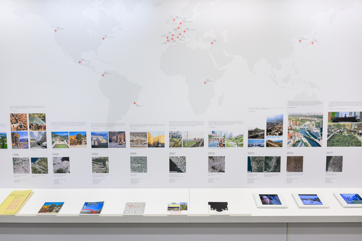 A wall displaying a large map of the world and a timeline of images above a shelf of books and video screens.