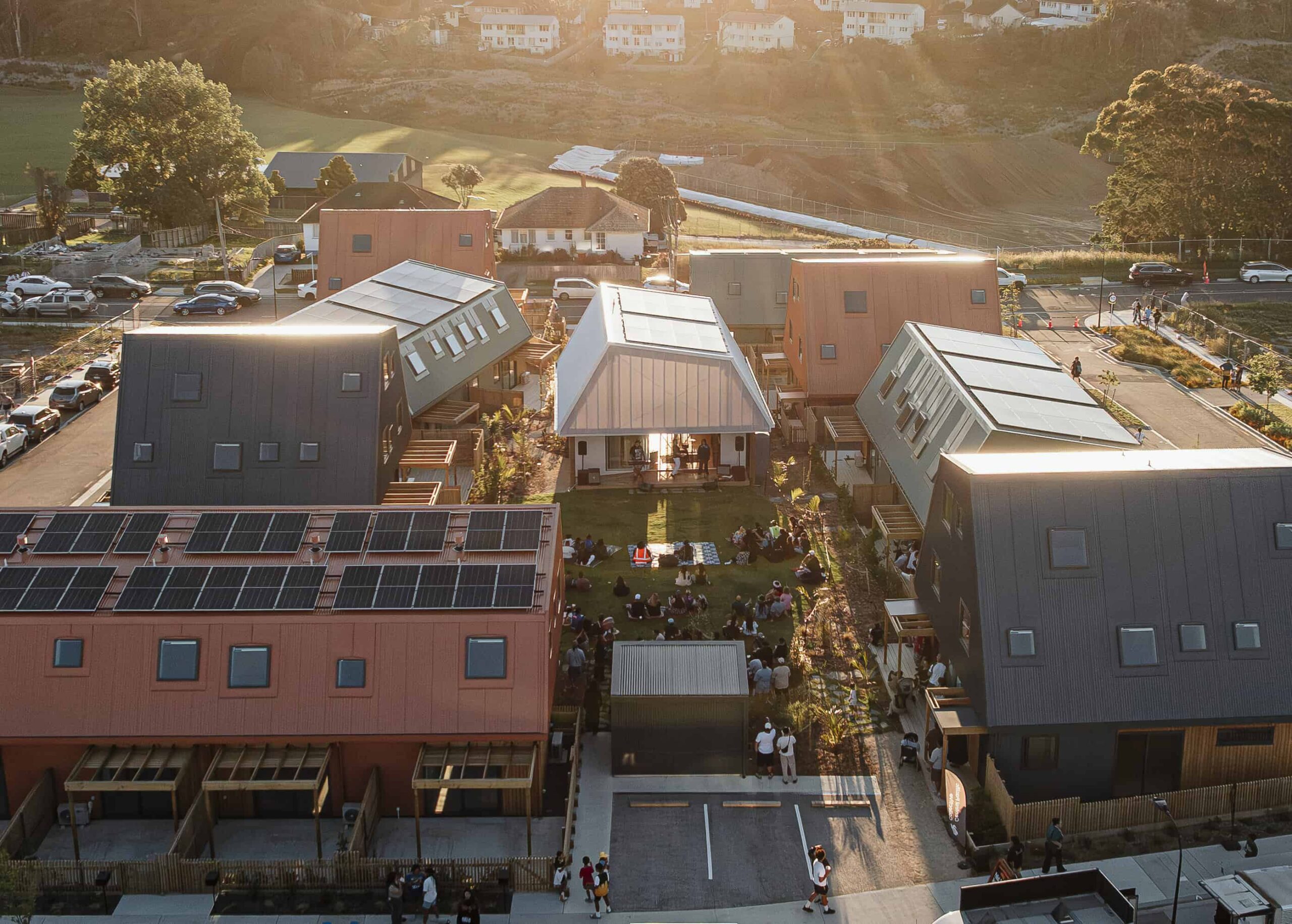 An aerial shot of a community gathered on a lawn between buildings with the sun shining down