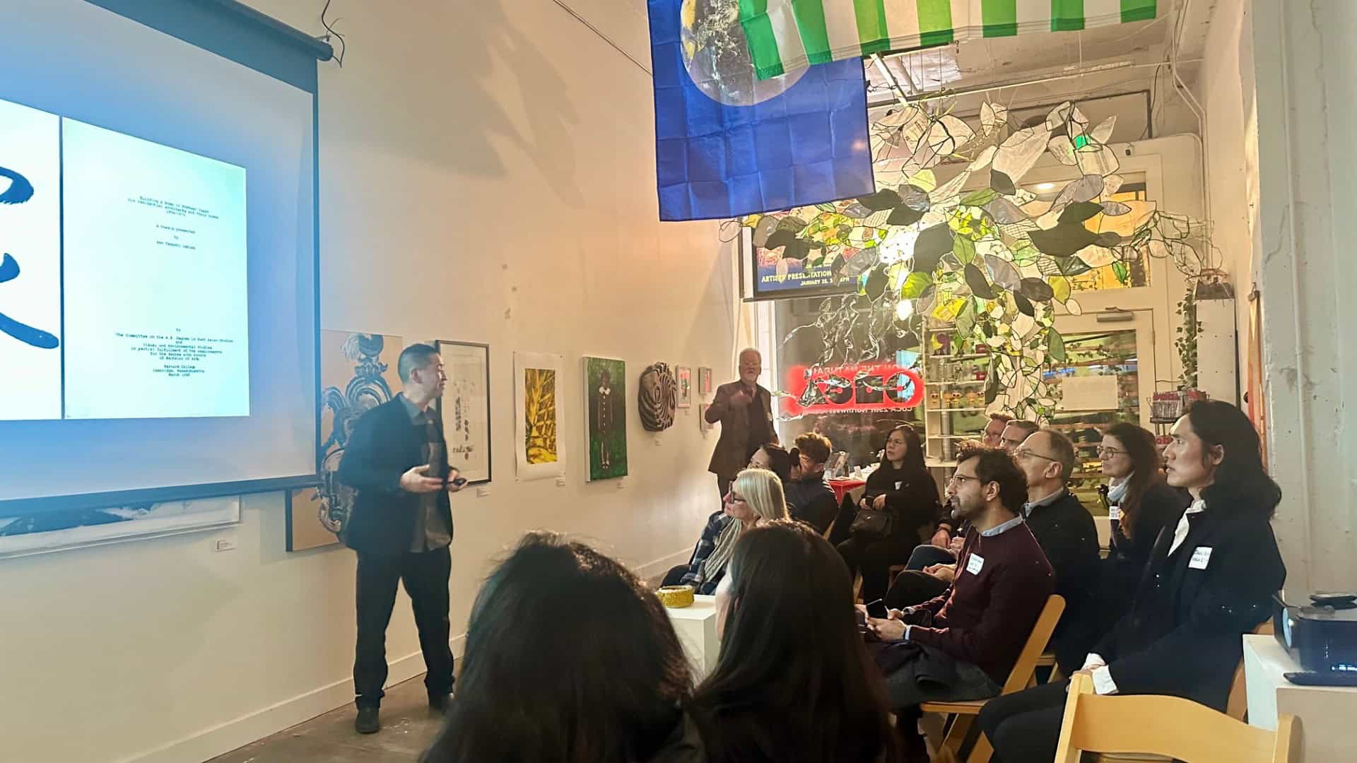 A presenter stands before a crowd of seated alumni