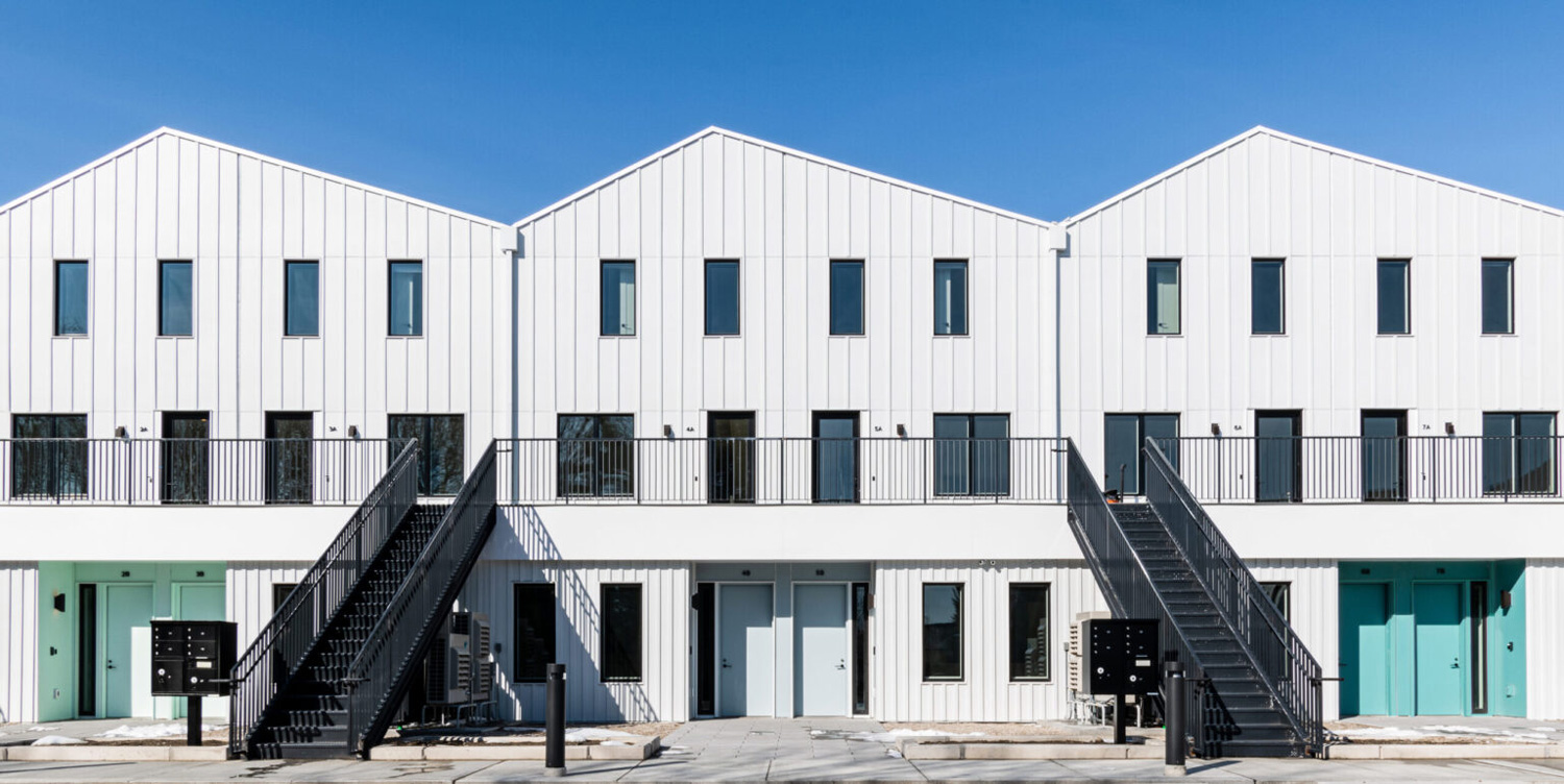 White housing with pitched roofs, blue doors and second floor balconies