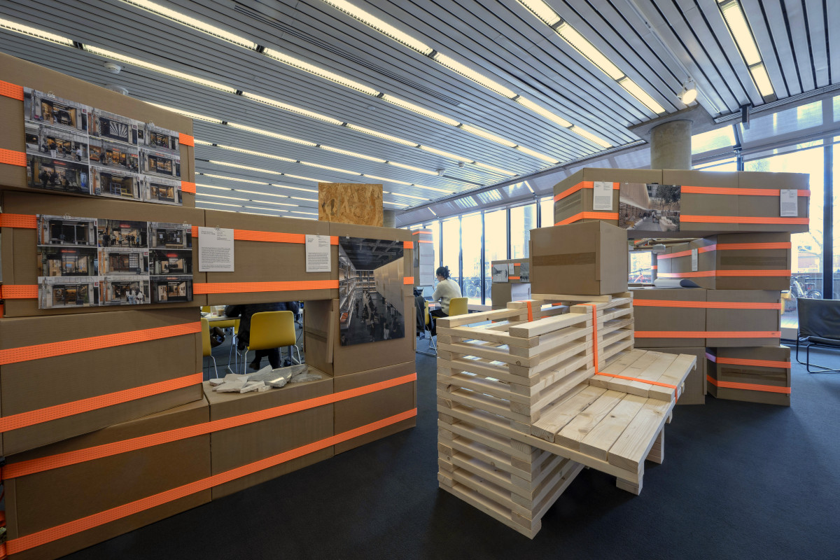 A bench built of lumber and ratchet straps surrounded by a temporary structure built from cardboard boxes and ratchet straps.