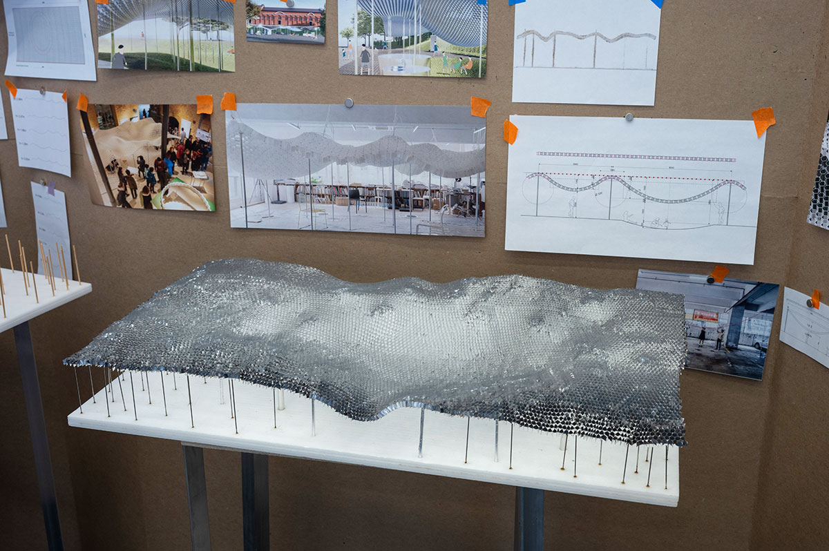 An architectural model in front of a brown wall with a variety of images taped to it.