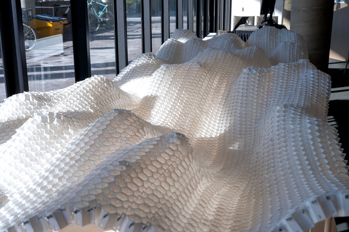 An architectural model of a long curvy form made of hexagonal shapes connected into a lattice.