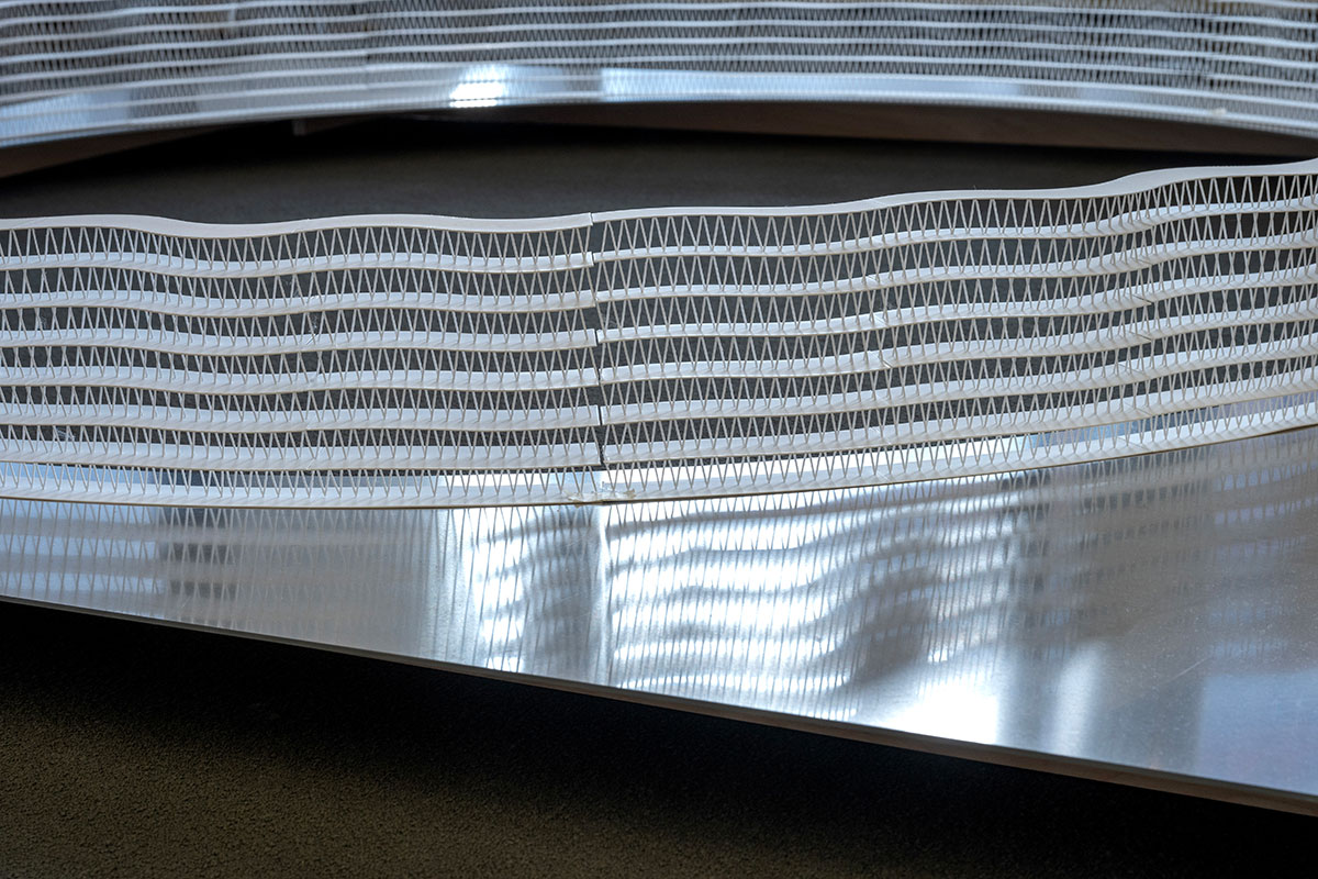 An architectural model of a circular wall of latticework displayed on an aluminum table top.