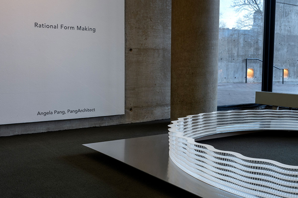 An architectural model of a circular wall of latticework on an aluminum table, on the floor of Frances Loeb Library. Behind it a wall says “Rational Form Making, Angela Pang, PangArchitect.”
