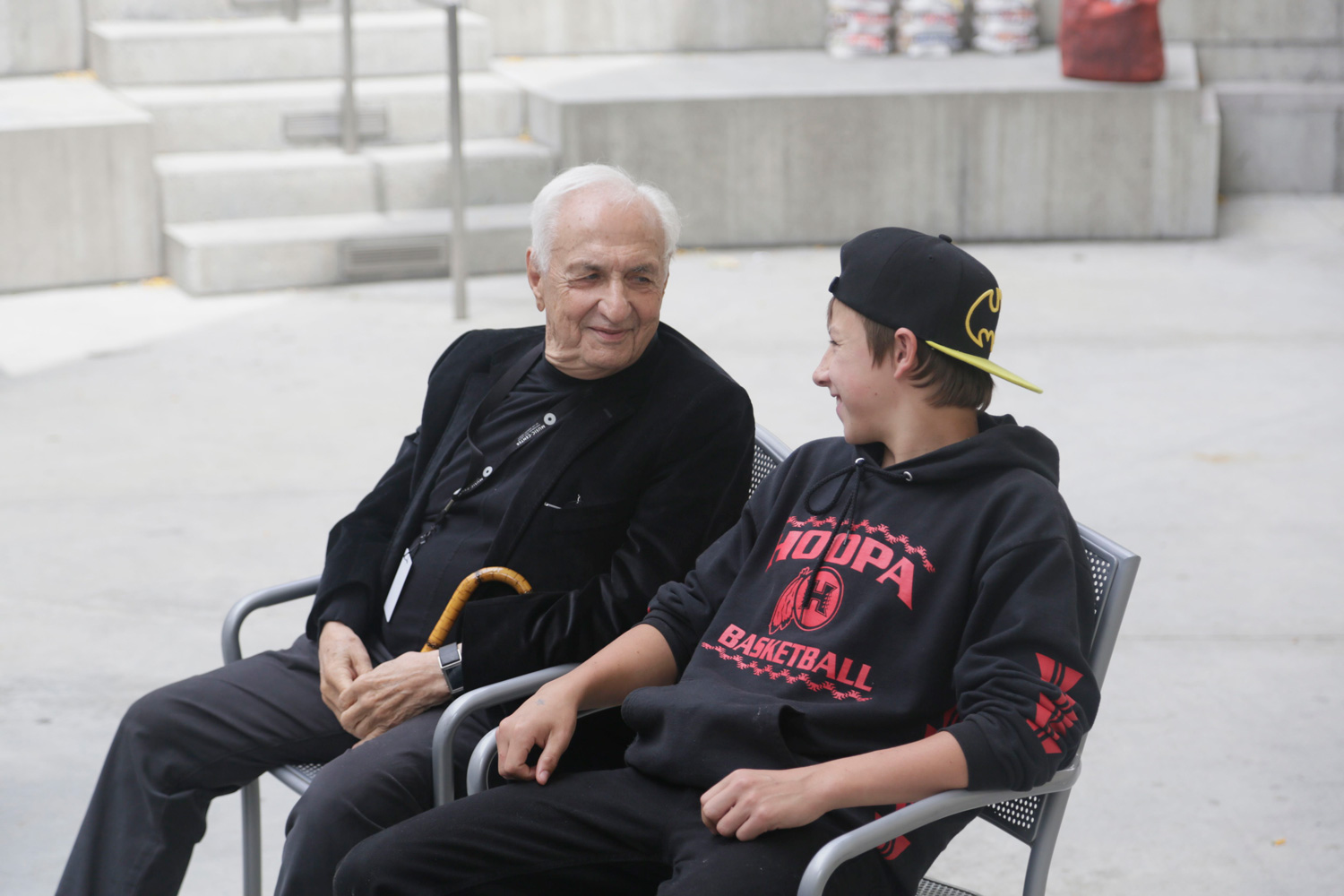 Frank Gehry and a student sit in chairs and appear to be in conversation.