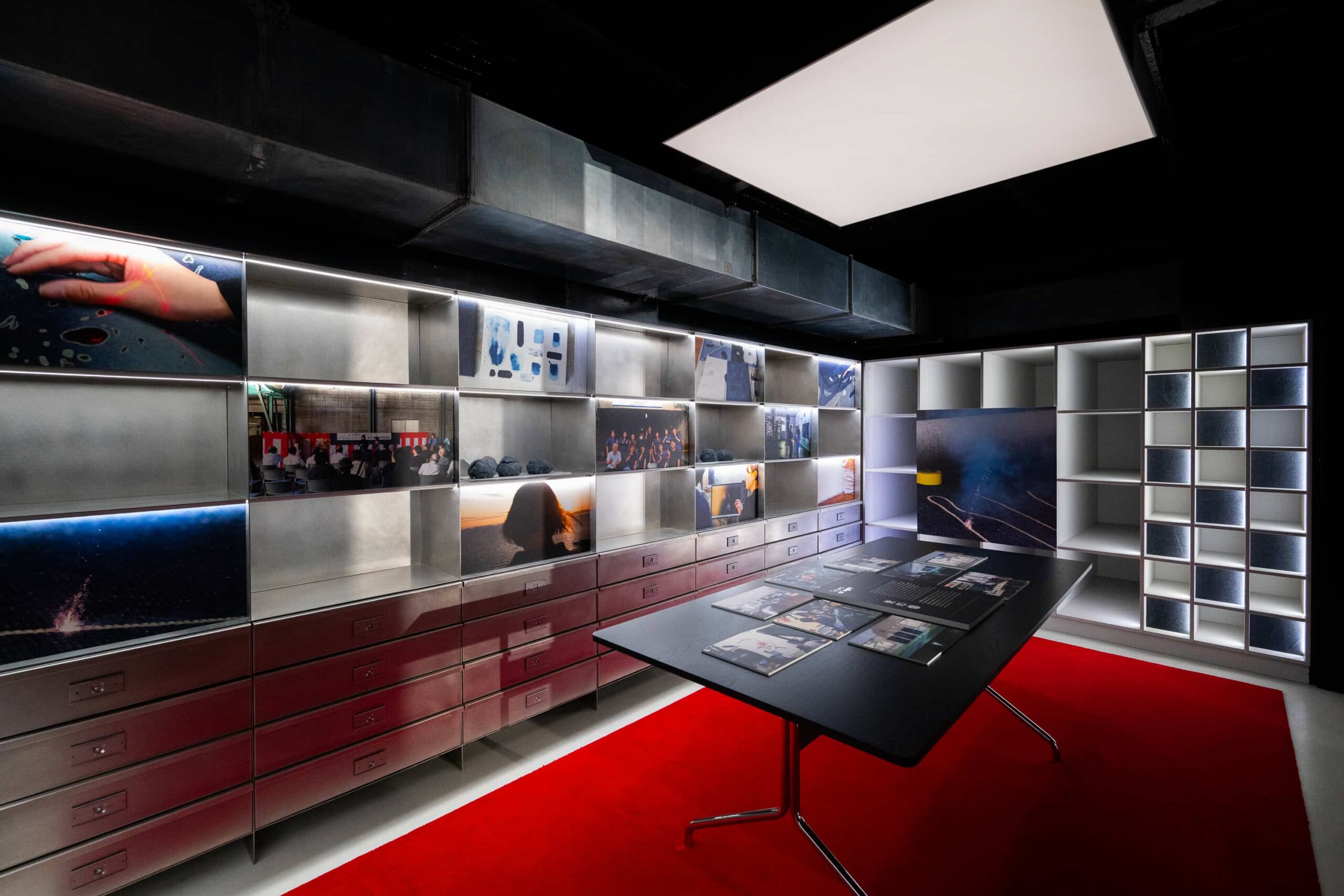 A dark room with with a bright overhead light shining above a black table and red carpet.