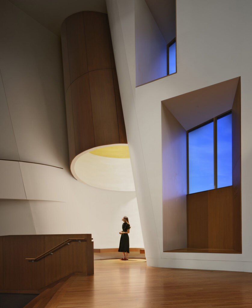 Woman standing under skylight and near windows.