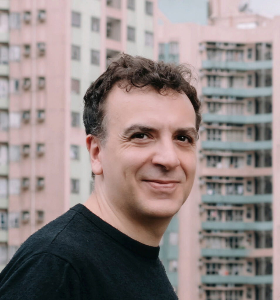 Man in black shirt smiles in front of skyscraper.