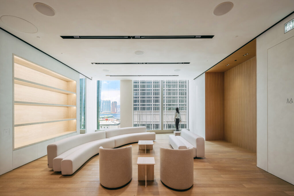 Sleek room with wood floors, white walls, lit built-in shelves, and cream colored seating.