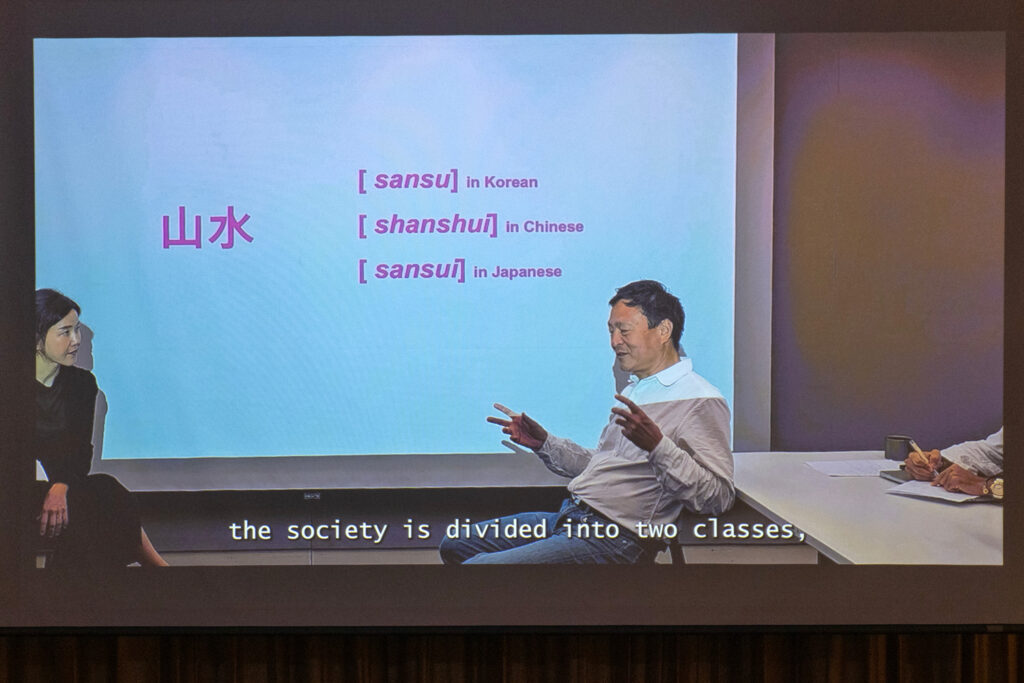 Landscape architect Kongjian Yu sits in front of a screen that says Sansu in Korea, Shanshui in Chinese, Sansui in Japanese. Subtitles read: "The society is divided into two classes"