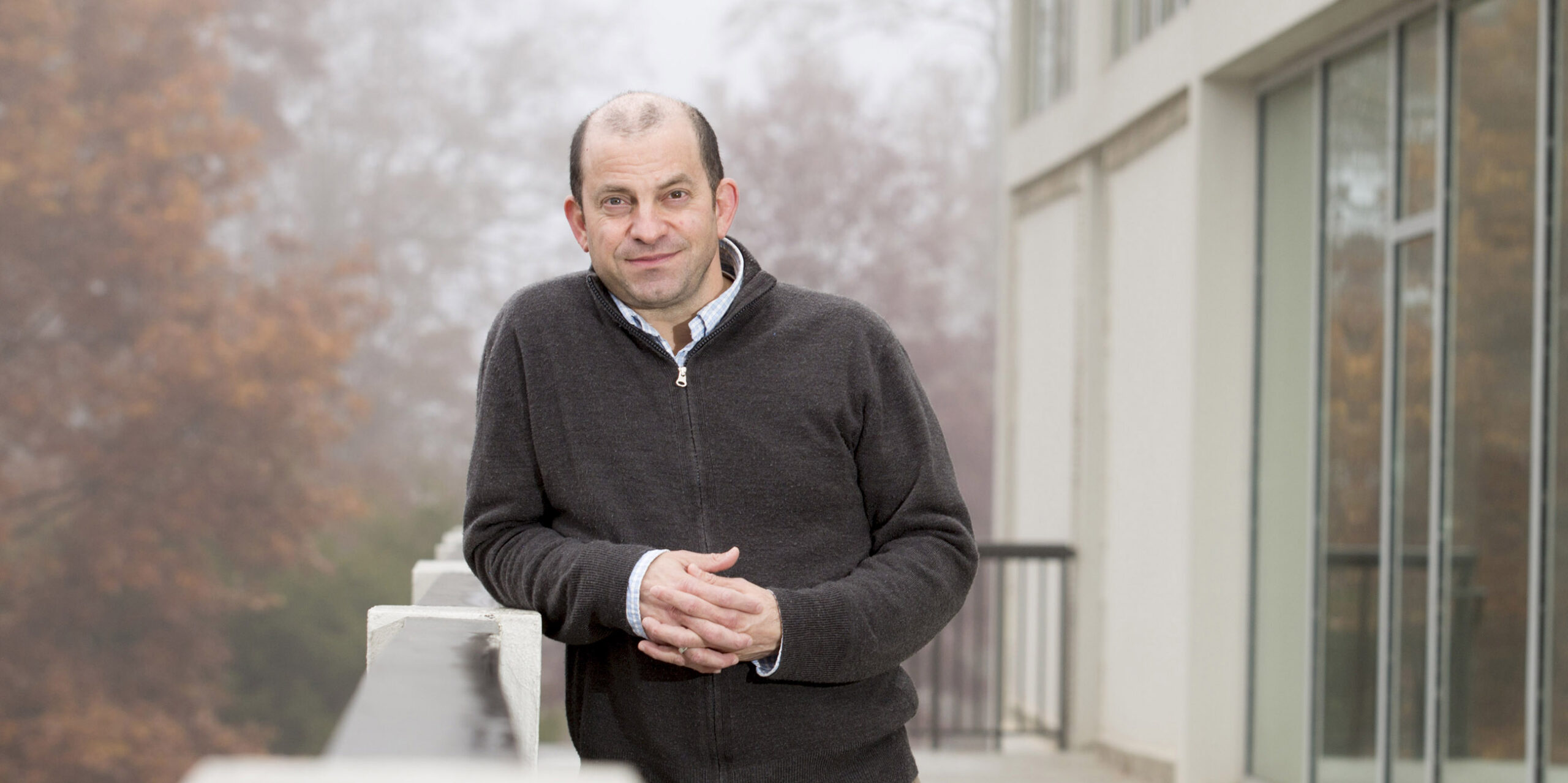 Stephen Ramos smiles on a balcony with fall trees in the background