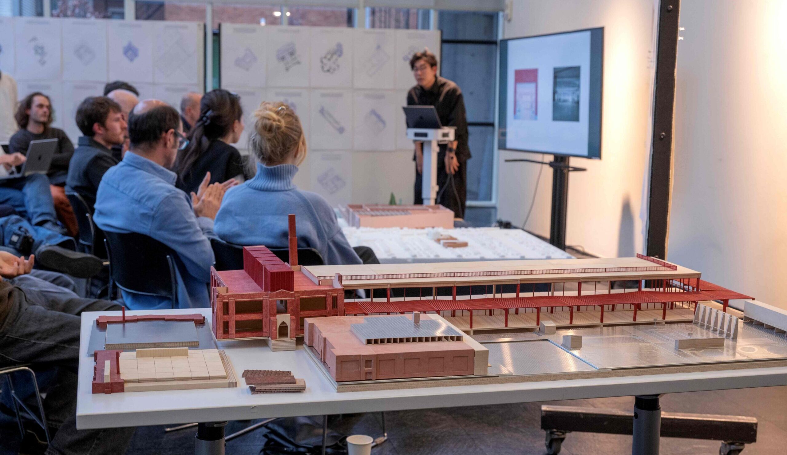 Architectural model foreground the view of a critique, with the jurors and student presentation in the background.