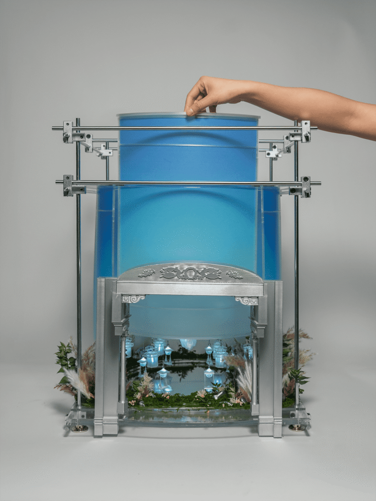 A hand is adjusting a model opera set with blue backdrops.