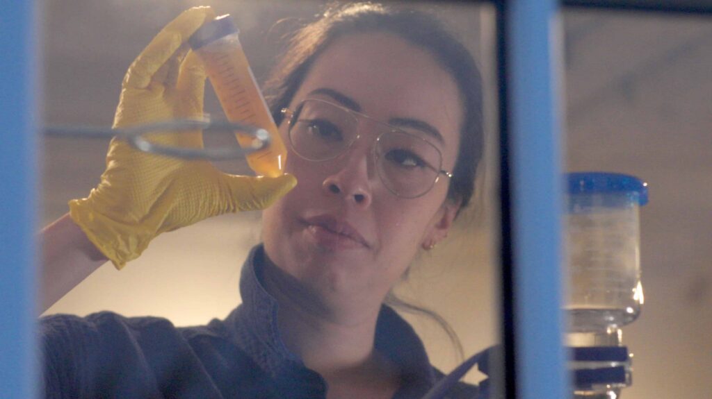 A woman in a lab holds a test tube with an inquisitive look