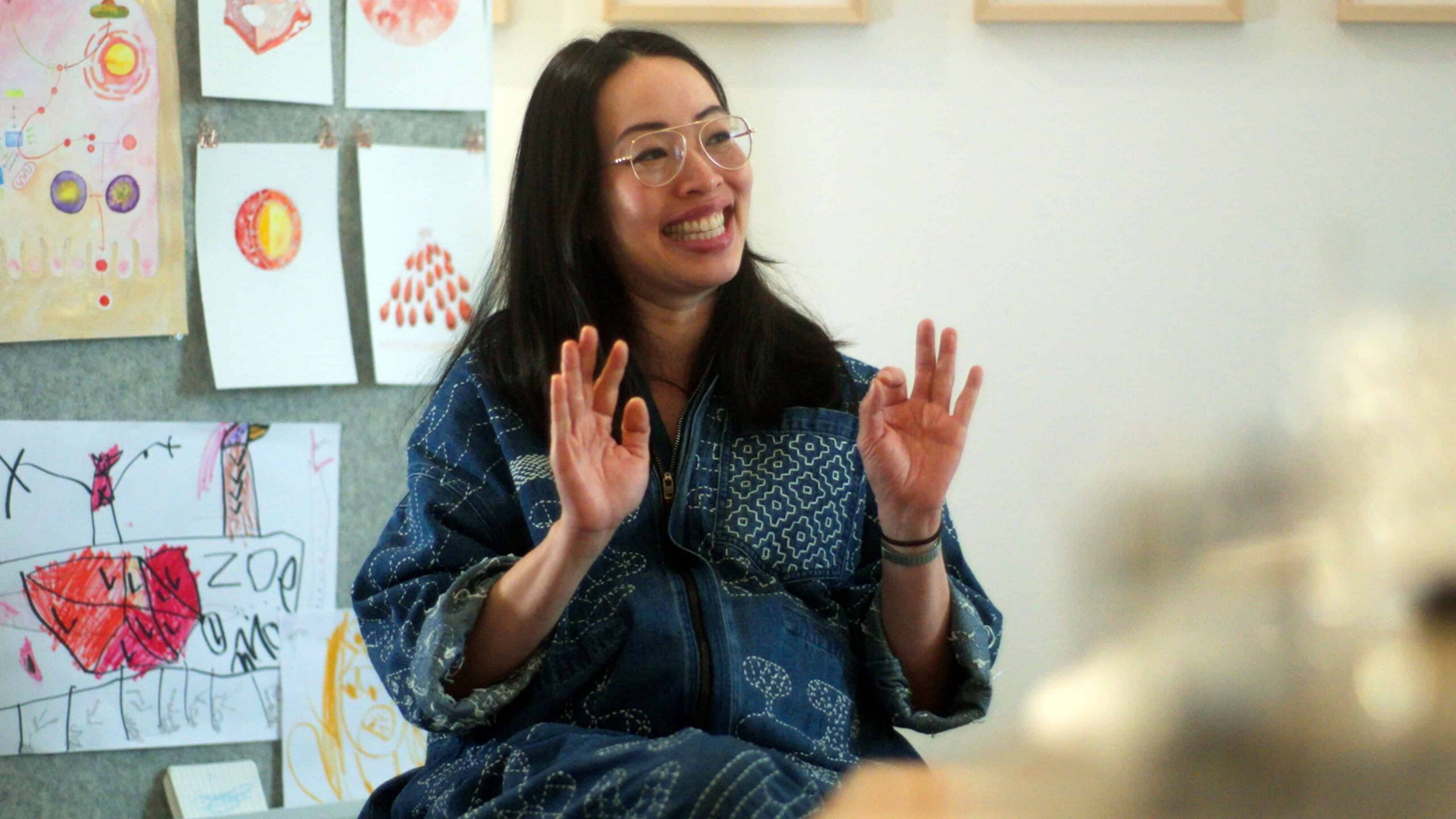 Ani Liu smiles mid-wave in front of children's artwork