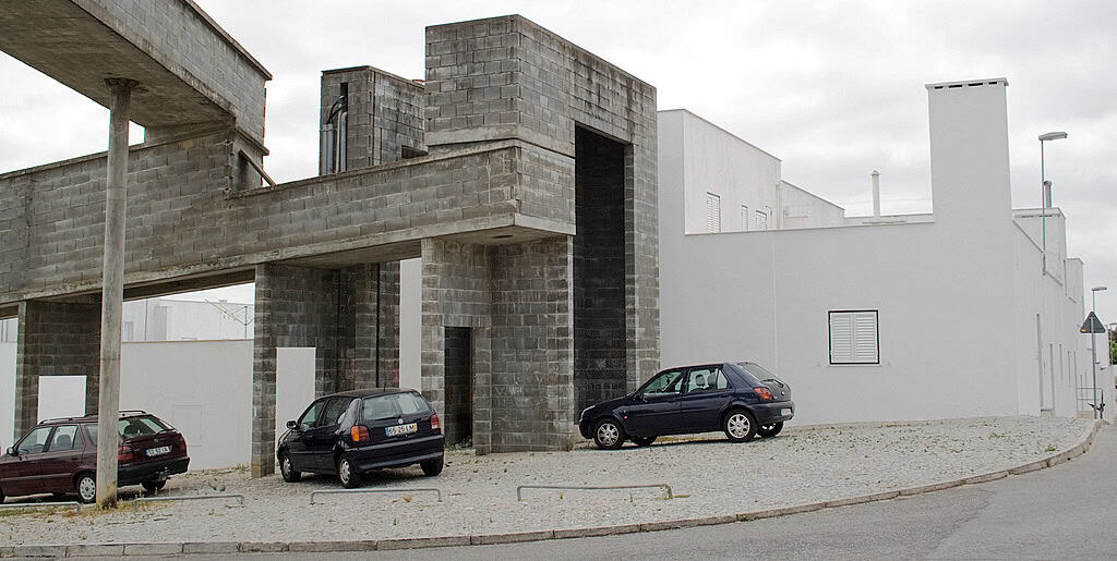 Exterior view of white housing structure and cement aqueduct. "Bairro Malagueira 2 (Evora)" by Torchondo from Sevilla, España is licensed under CC BY 2.0.