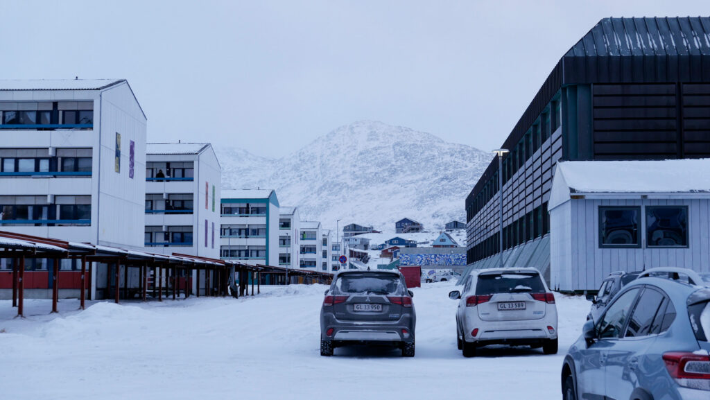 Cars and buildings in town with snowy mountains.