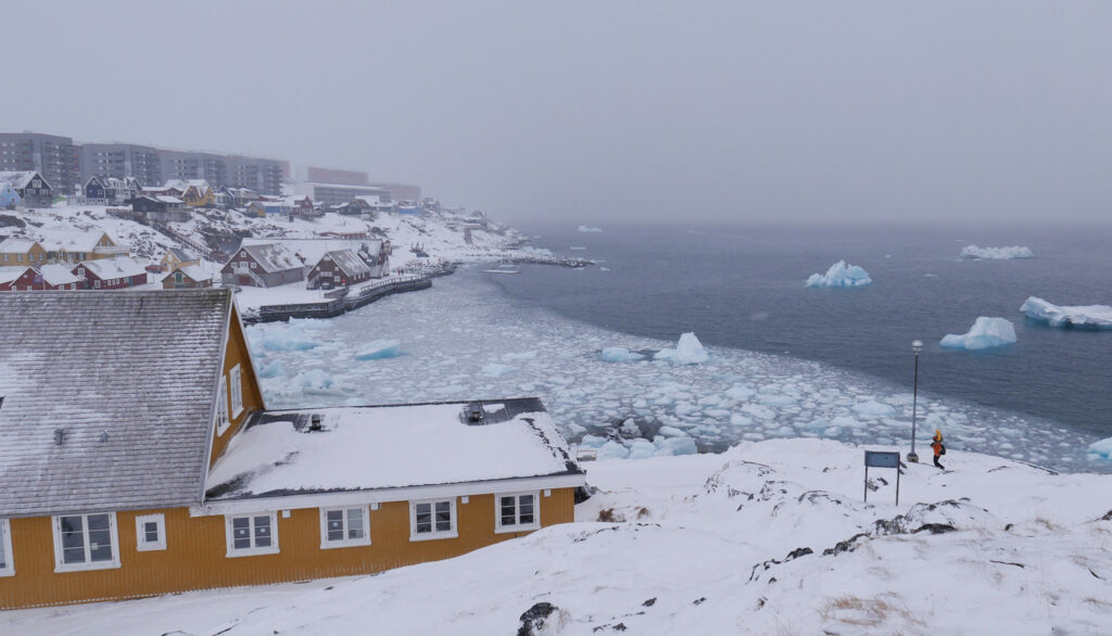 View of coastline with yellow house, snow, freezing harbor. and city in the background