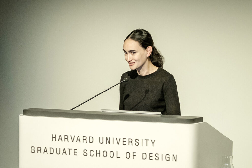 Woman with dark hair and dark shirt talks into microphone at a podium.