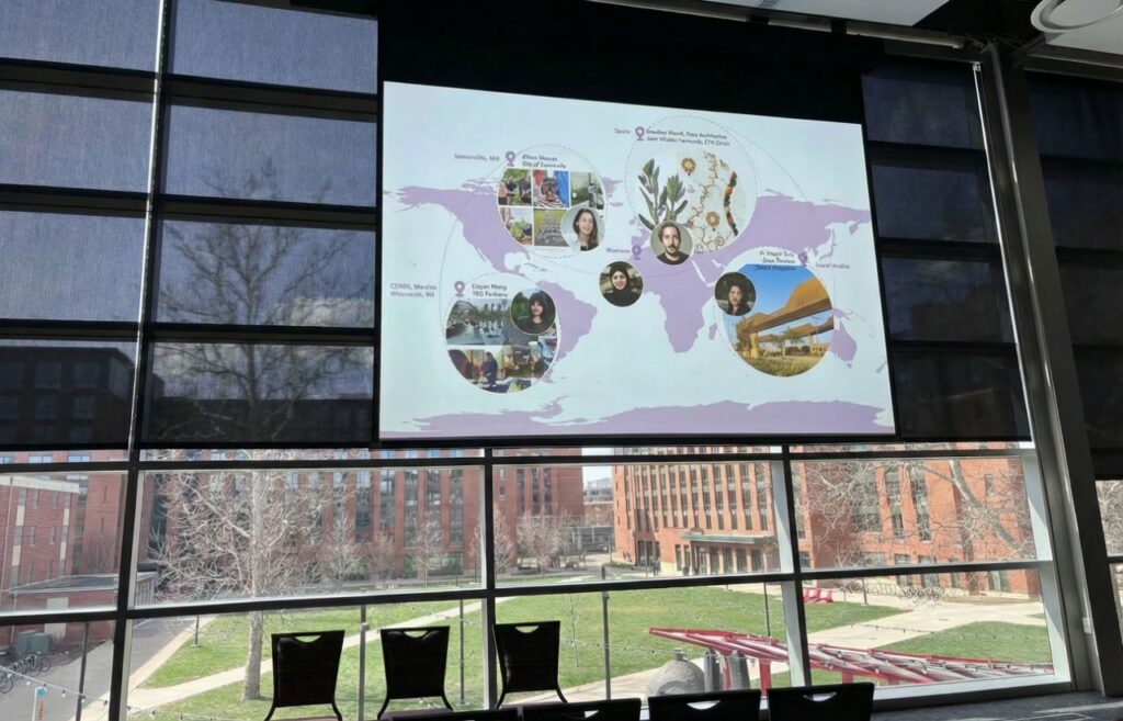 A projector in a conference room shows a map and headshots of speakers