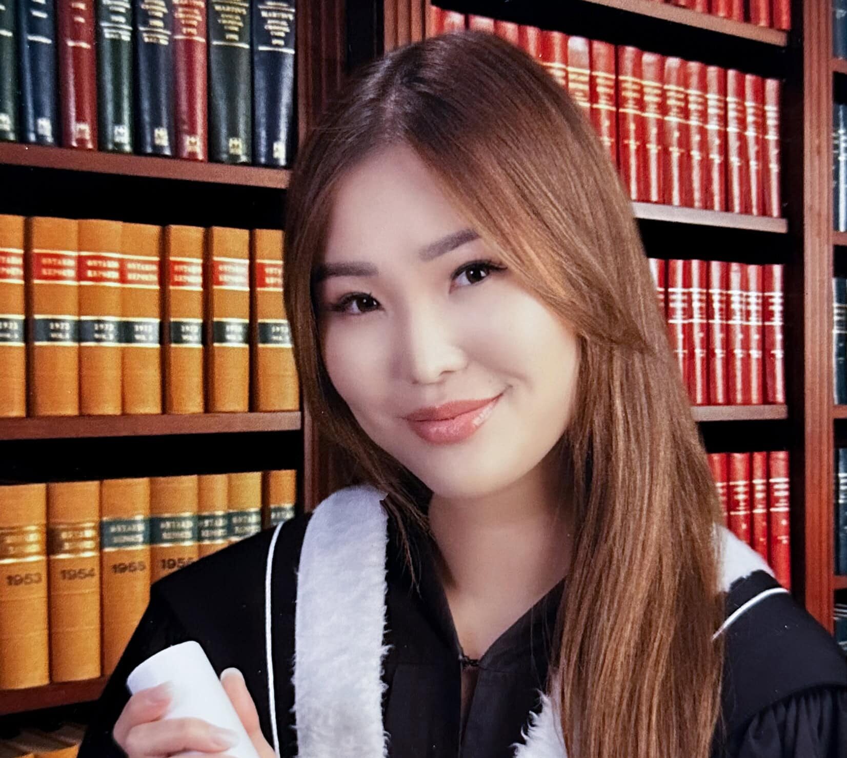 Enkhjin Ross photo at Commencement with a background of books.