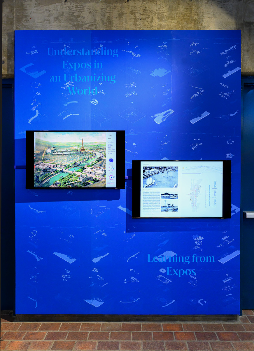 Two video monitors on a wall displaying historical images of expos.