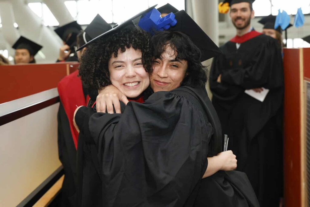 Two GSD graduates hug while smiling at the camera.