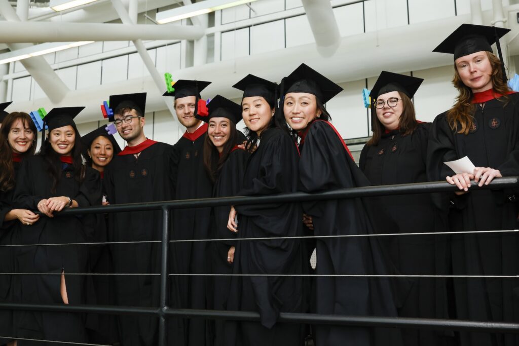 A group of GSD graduates stand by a railing while smiling at the camera.