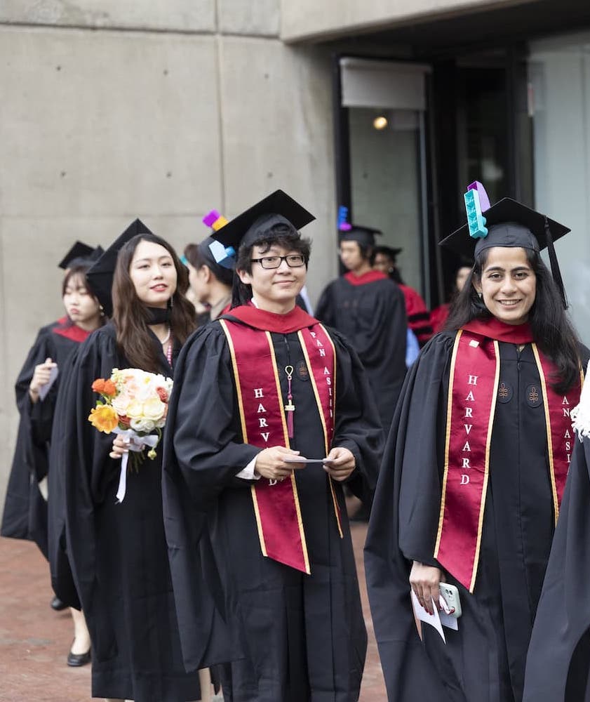 GSD graduates smile at the camera as they walk in a single file line. 