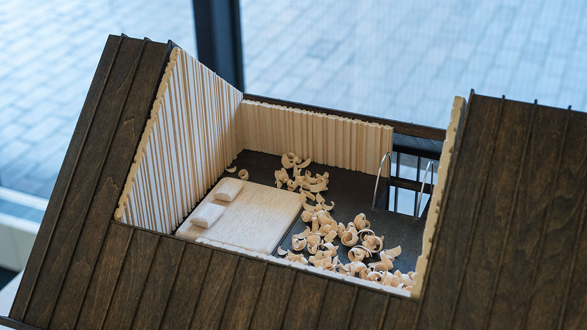 Detail of a wooden architectural model showing a roof with a cutout into a bedroom made of wood and wood shavings.