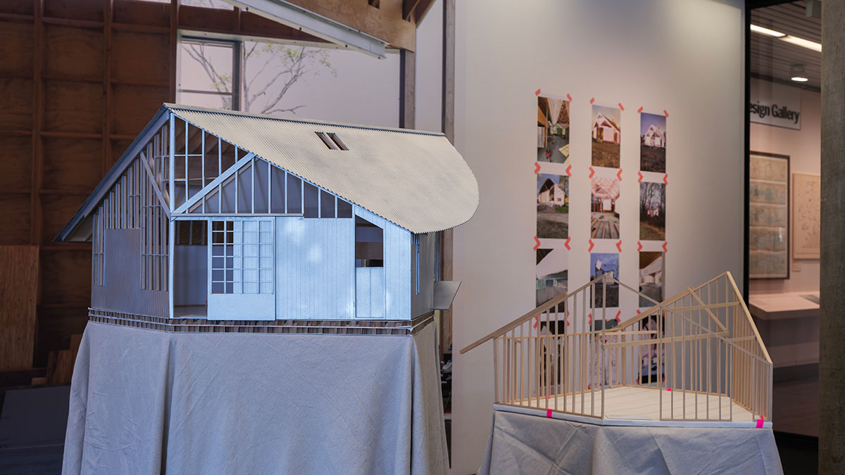 Two architectural models of buildings in front of a wall with a large mural and smaller images of buildings.