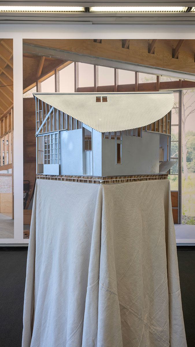 An architectural model of a house on top of a pedestal draped with canvas cloth.