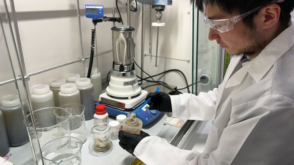 A man in a laboratory scoops some gray substance out of a jar.