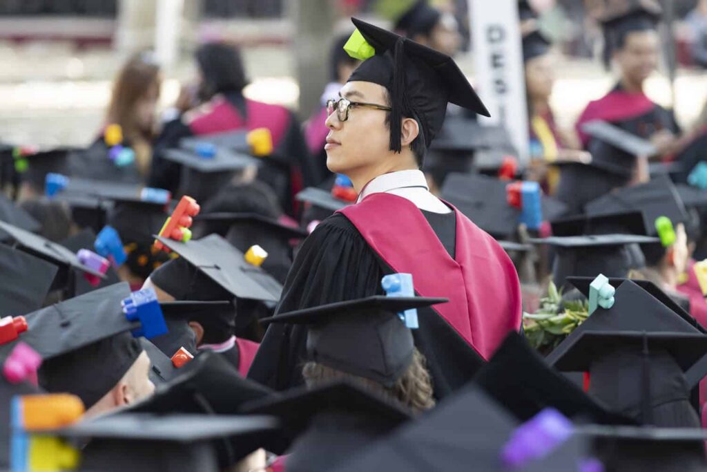 A GSD graduate stands among a crowd wearing cap and gown.