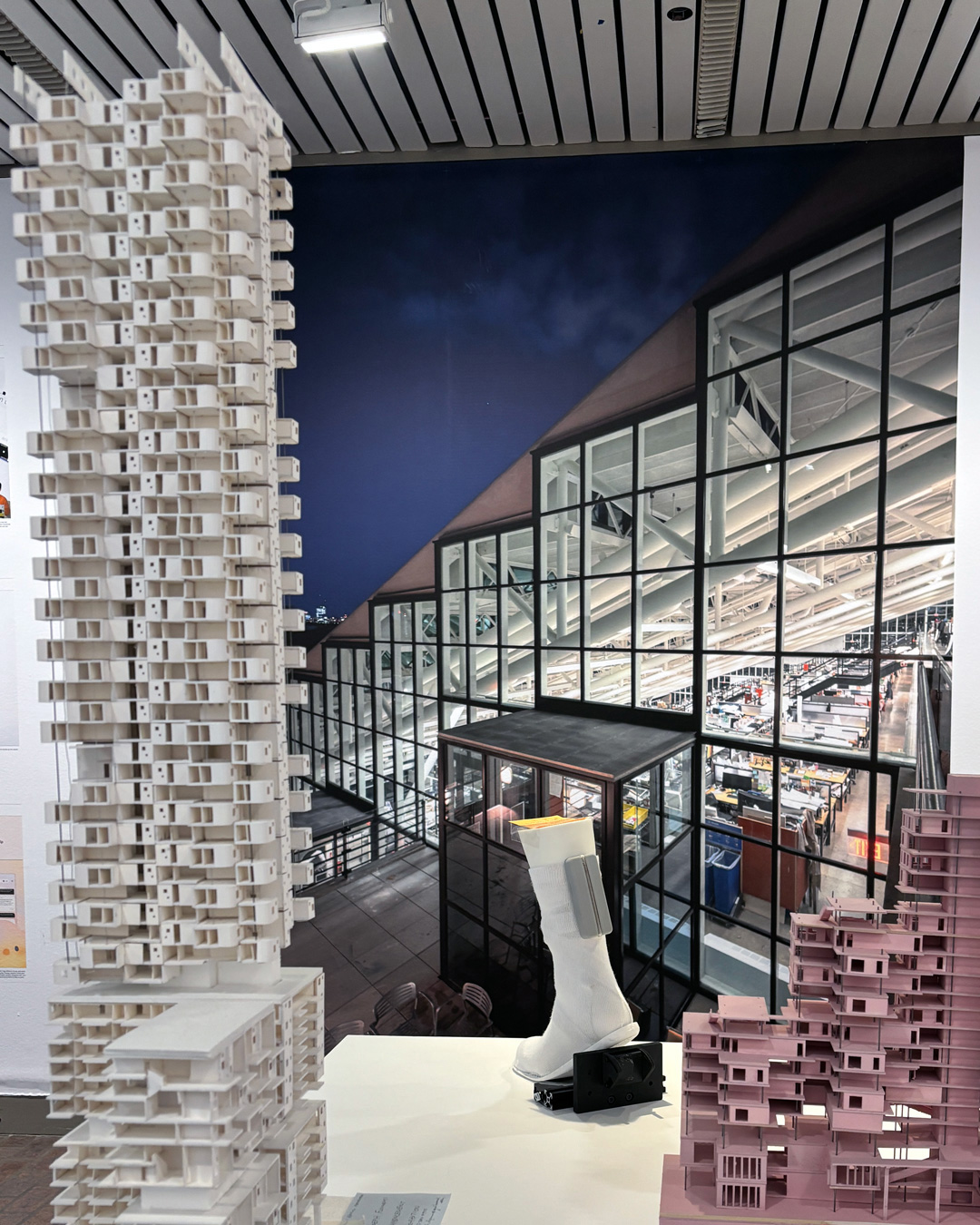 A group of architecture models as well as a white sock sit on a table in front of a photograph of Gund Hall.