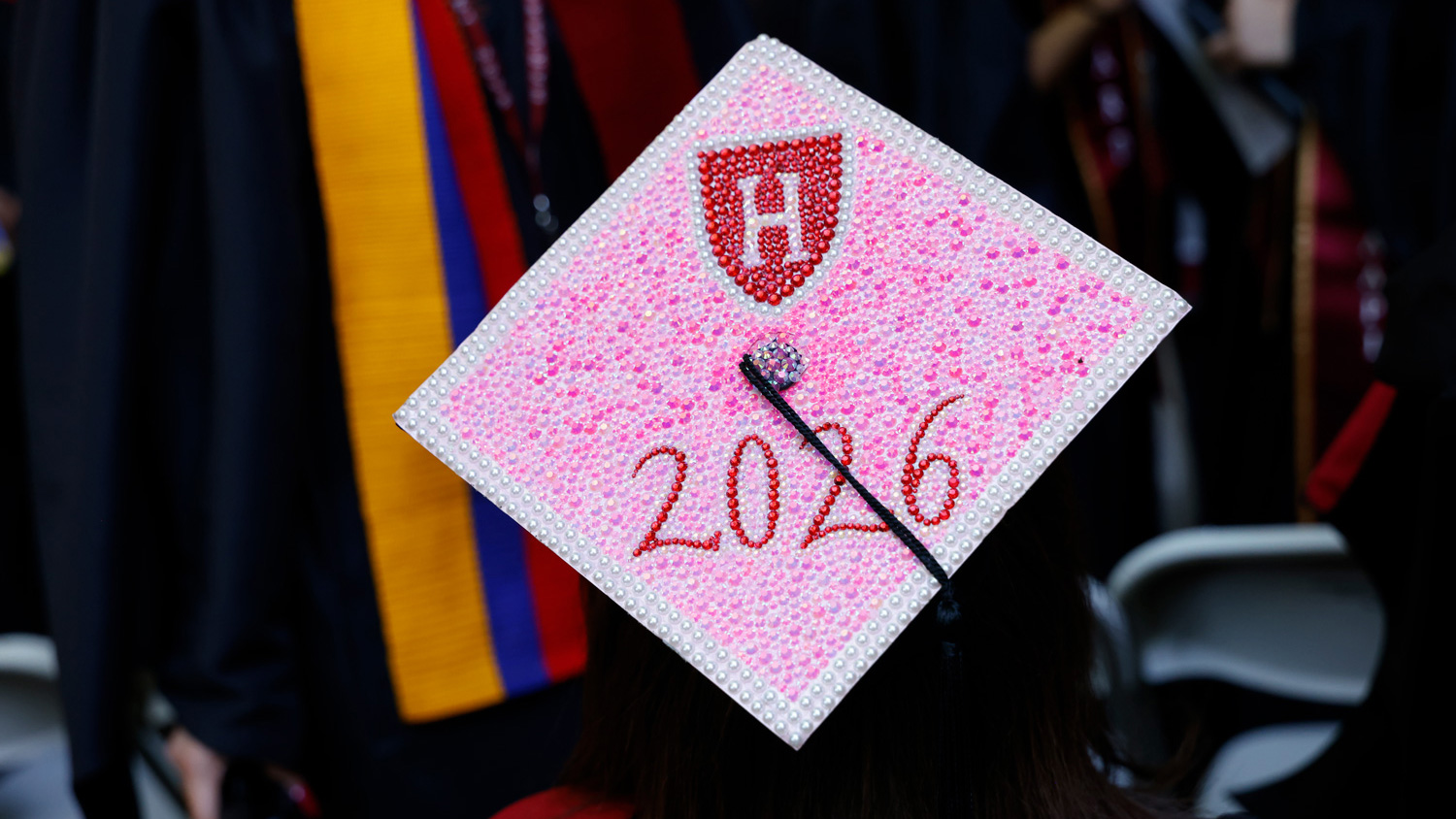 A graduation cap decorated with pink shimmering stones to spell out Harvard 2026.