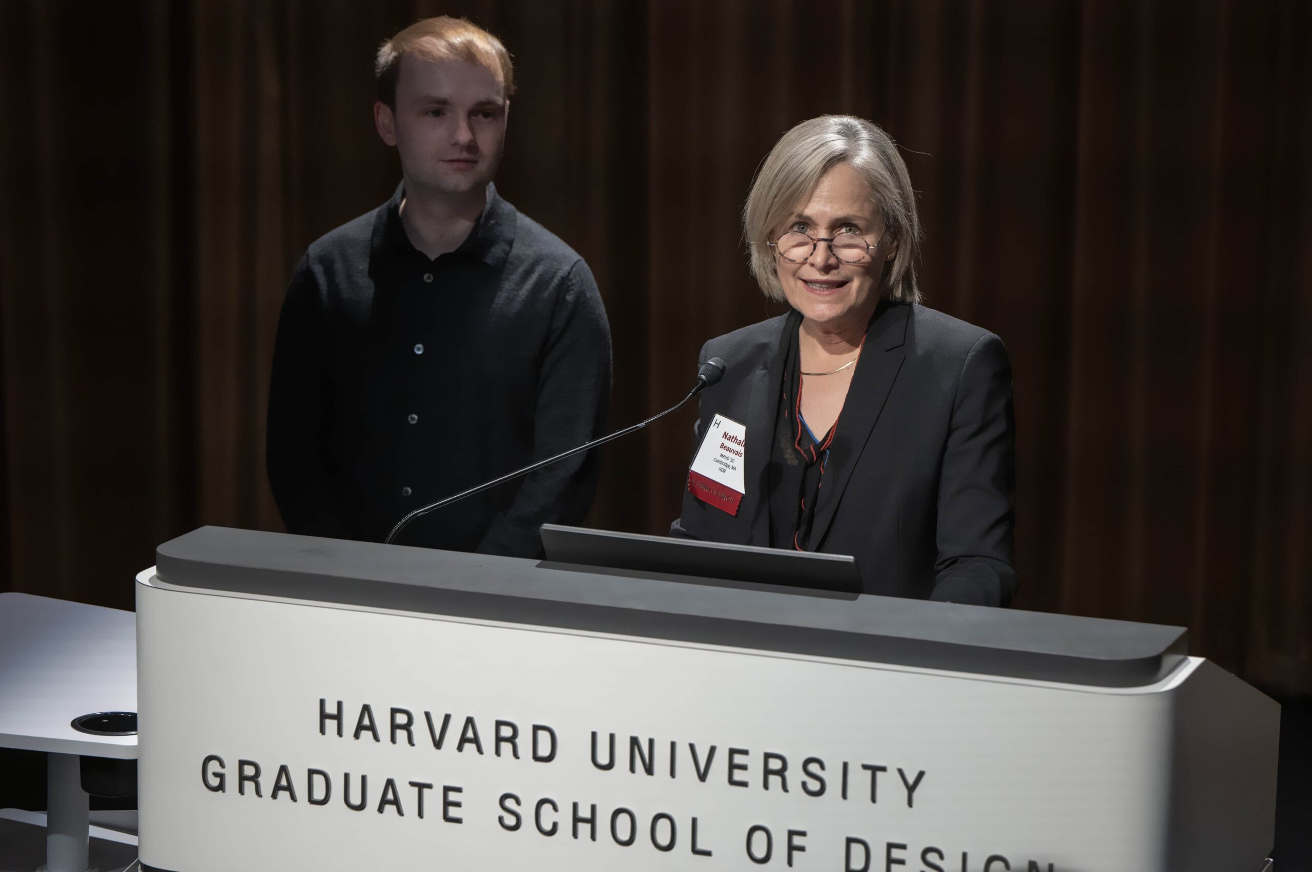 Two people stand behind a podium that reads "Harvard University Graduate School of Design"