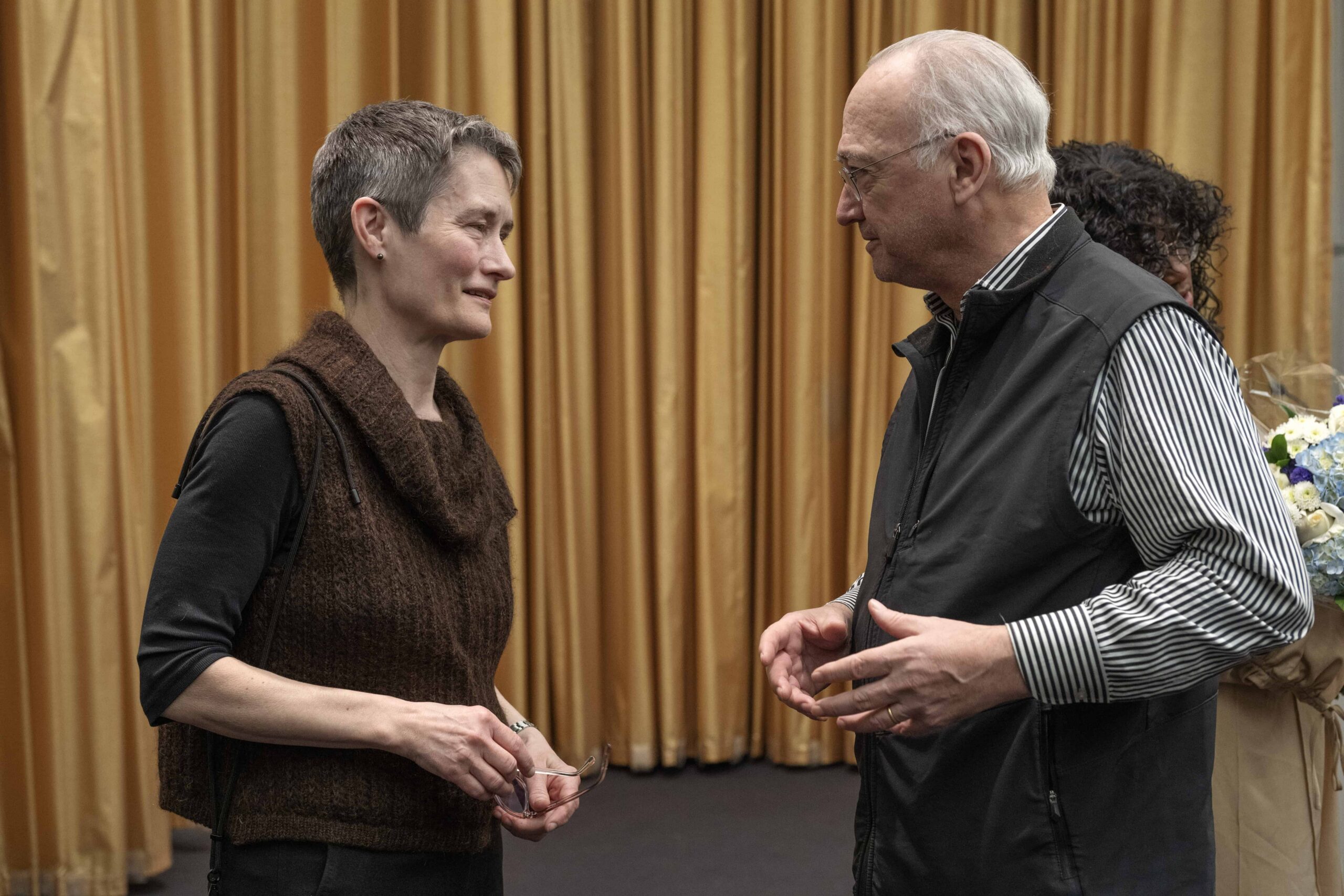 Two people having a discussion in front of a gold curtain