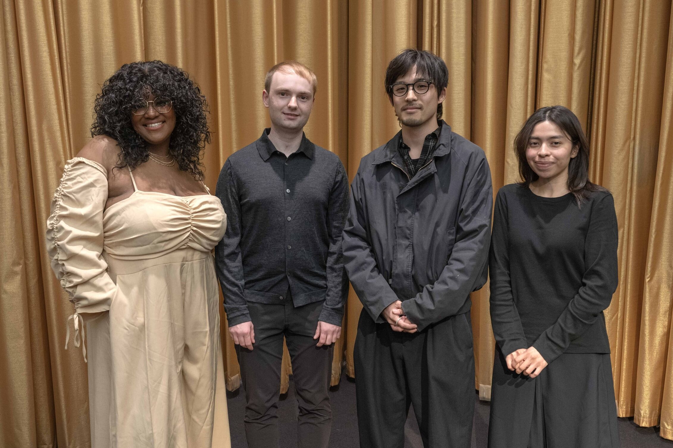Four students stand in front of a gold curtain