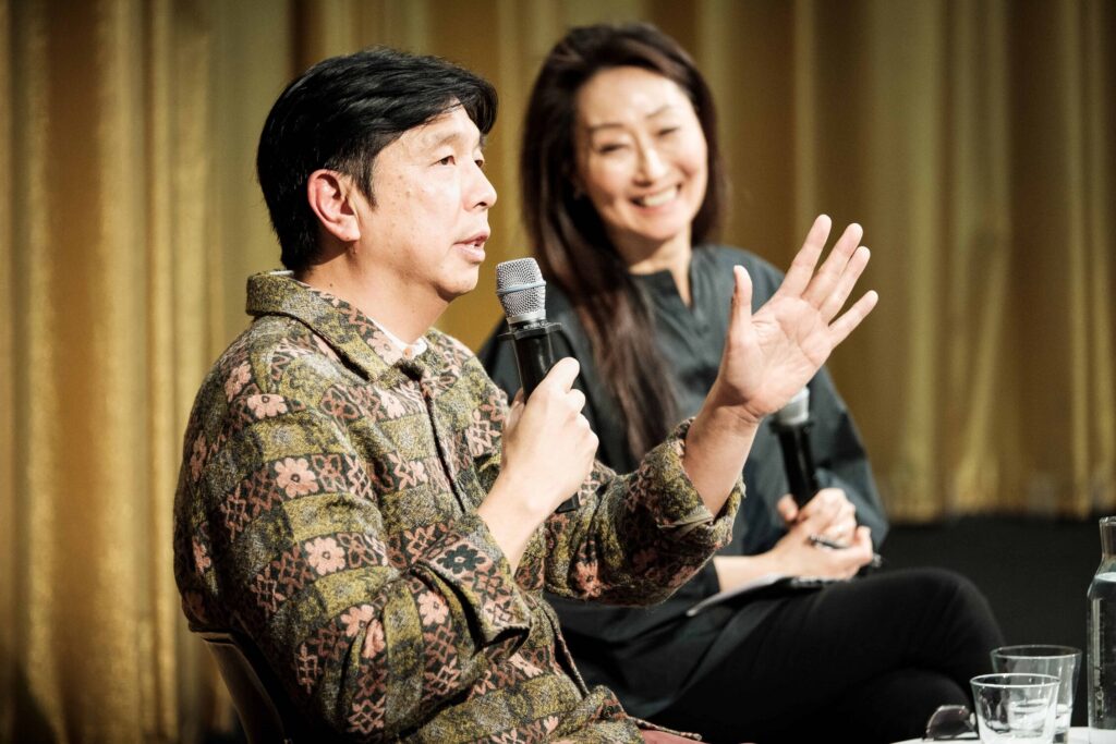 Chat Chuenrudeemol and Grace La sit in front of a gold curtain during a panel at the GSD.